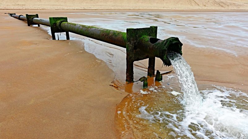 A pipe expelling water on a beach. 